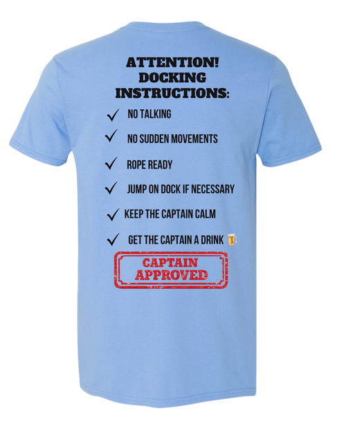 A light blue short-sleeve t-shirt shown from the back, featuring a humorous checklist titled 'ATTENTION! DOCKING INSTRUCTIONS:' in black text, with a red 'CAPTAIN APPROVED' stamp graphic at the bottom.