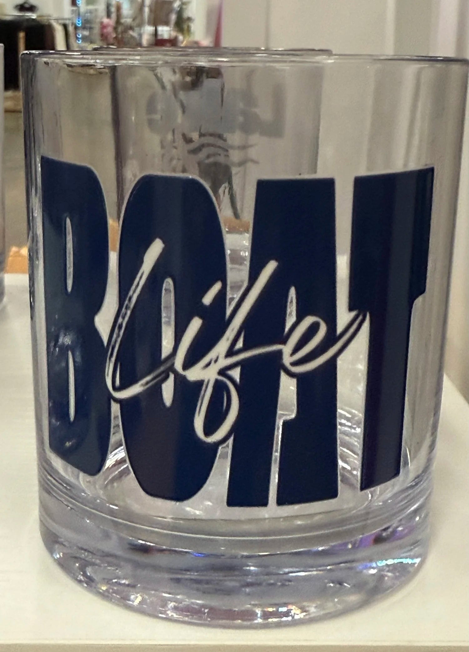 A clear glass tumbler with a thick base featuring the word 'BOAT LIFE' in large navy blue letters, with 'life' written across the center in white cursive script.