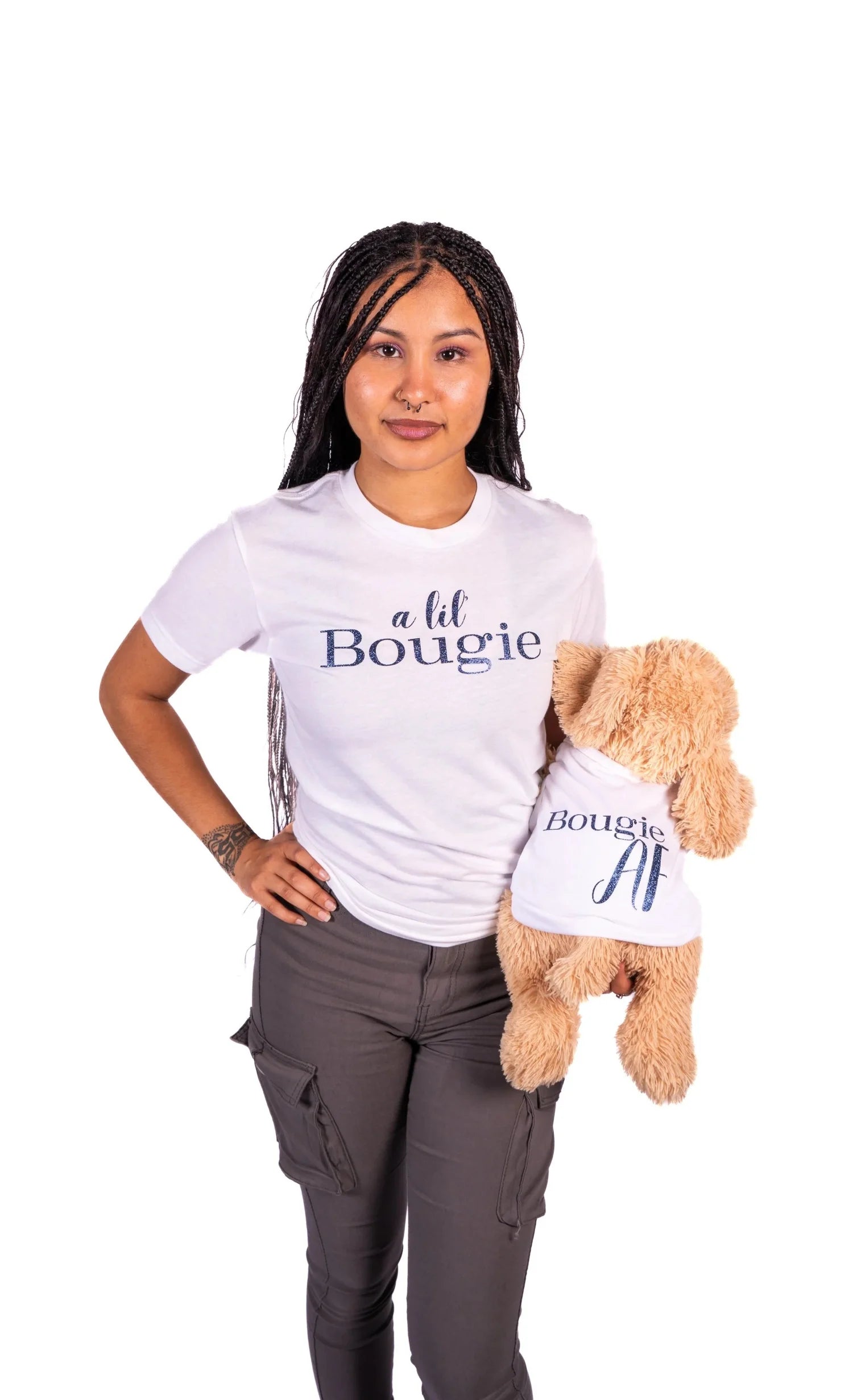 A woman with long dark hair wearing a white graphic t-shirt that says 'a lil Bougie' and dark gray pants, holding a brown plush dog wearing a matching t-shirt, with wording Bougie AF
