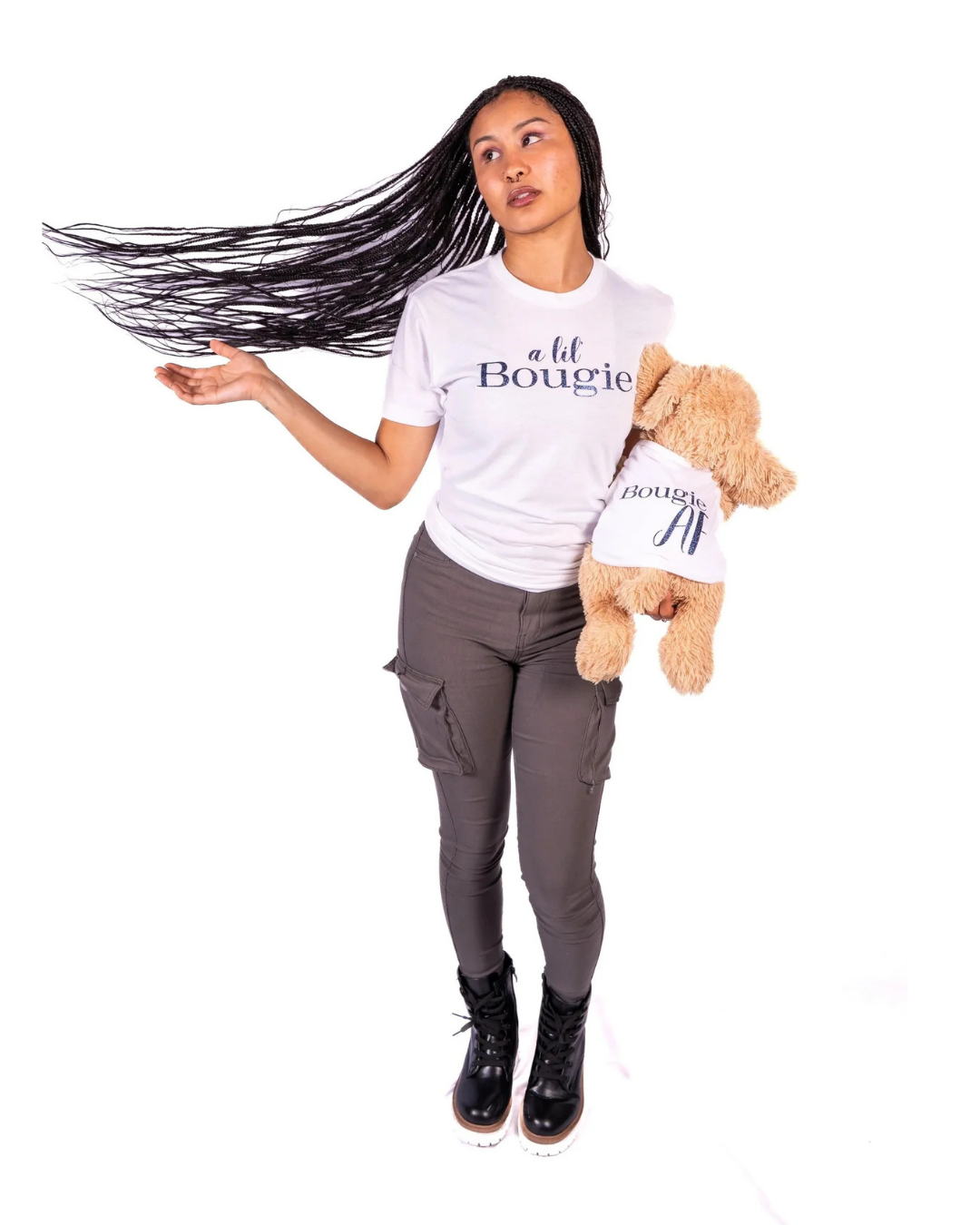 A woman with long dark hair wearing a white graphic t-shirt that says 'a lil Bougie' and dark gray pants, holding a brown plush dog wearing a matching t-shirt, with word Bougie AF