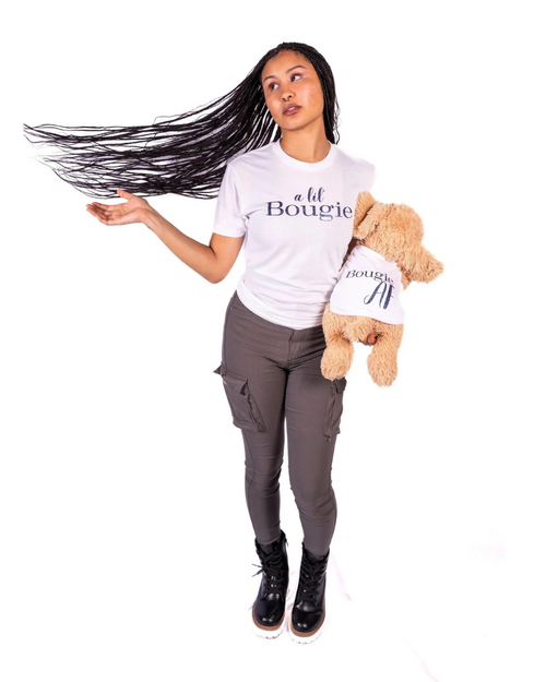 A woman with long dark hair wearing a white graphic t-shirt that says 'a lil Bougie' and dark gray pants, holding a brown plush dog wearing a matching t-shirt, with word Bougie AF