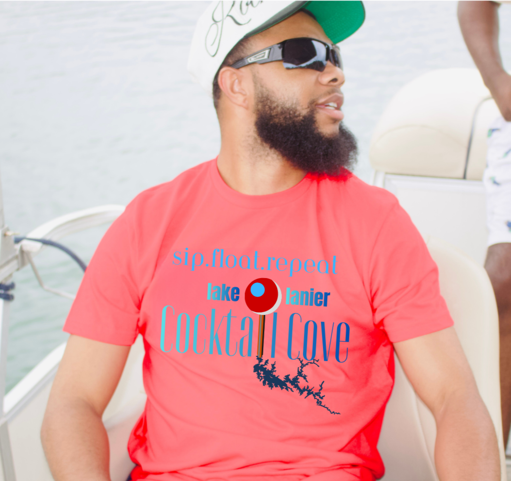 A man wearing a red graphic t-shirt on a boat. The shirt features a blue and red graphic that reads 'sip. float. repeat Lake Lanier Cocktail Cove with a graphic of the lake and a pin showing where the cove is