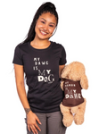 A woman wearing a black graphic t-shirt that reads 'MY DAWG IS MY DOG' holds a plush tan dog toy wearing a brown shirt that reads 'MY HUMAN IS MY DAWG' against a plain white background.