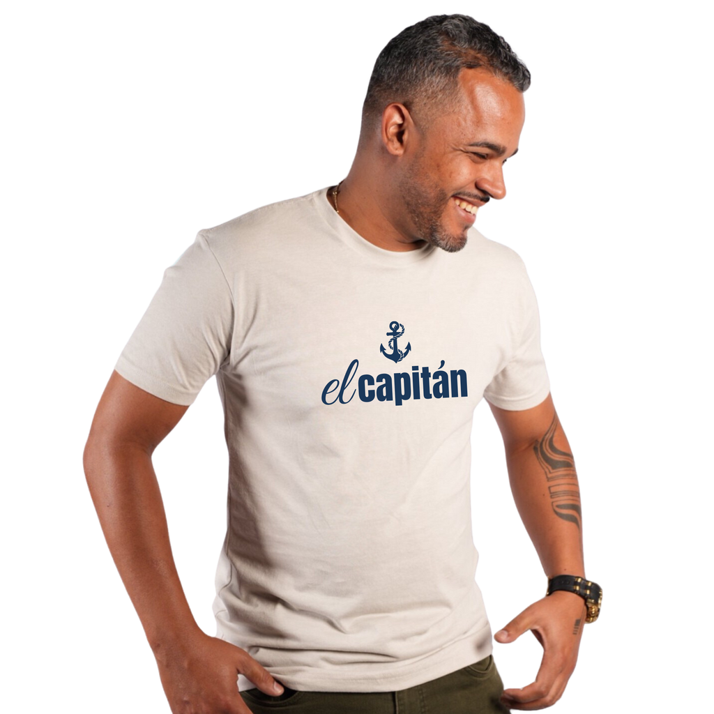 A man wearing a light beige crewneck t-shirt with a navy blue anchor graphic and the text 'el capitán' printed on the chest, set against a plain white background.