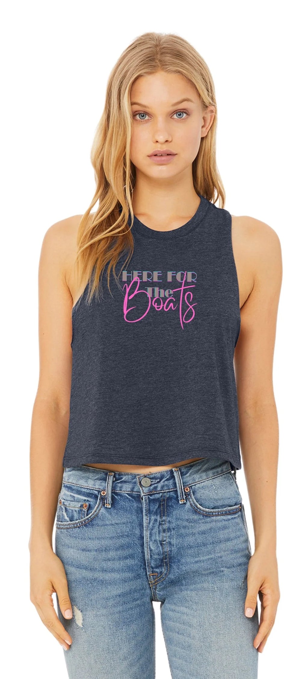 A woman modeling a dark heather gray sleeveless crop tank top with a graphic that reads 'HERE FOR THE Boats' in white and pink, paired with blue jeans against a plain white background.