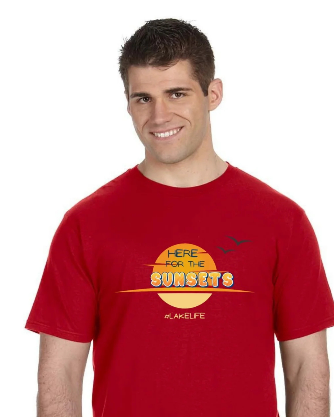 A smiling man wearing a red short-sleeve t-shirt with a yellow and orange graphic on the chest that reads 'HERE FOR THE SUNSETS' and 'LAKELIFE'.