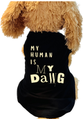 A black pet shirt with the text 'MY HUMAN IS MY DaWG' printed in cream lettering, shown on a brown plush dog toy against a white background.