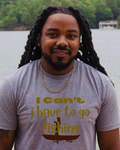 A man with long black dreadlocks stands outdoors by the water wearing a heather gray t-shirt with a gold graphic that reads 'I Can't i have to go fishing' above a fishing rod and boat illustration.