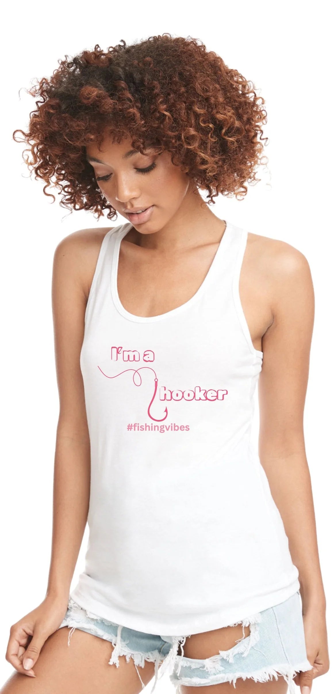 A woman with curly brown hair wearing a white racerback tank top with pink text that reads 'I'm a Hooker' and '#fishingvibes', paired with light blue denim shorts, against a plain white background.