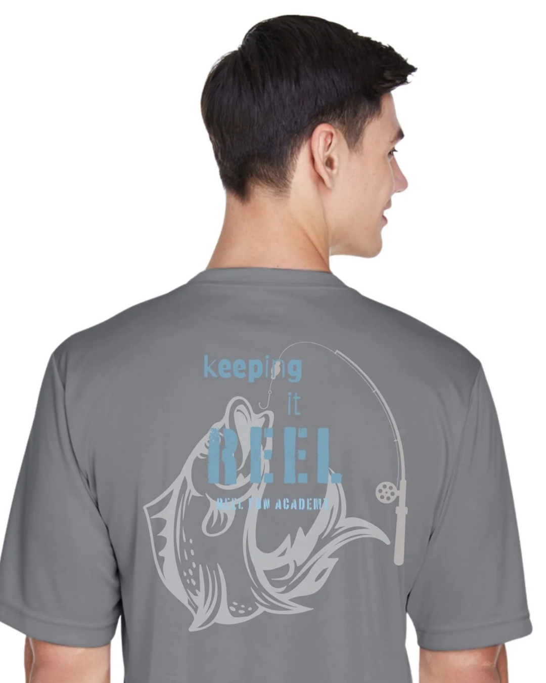 A man shown from the back wearing a gray t-shirt with a light blue and white graphic that reads 'keeping it REEL FISHING ACADEMY' with a fish and fishing rod design.