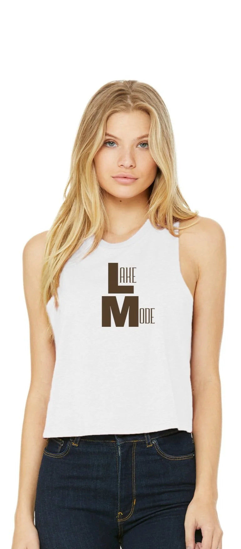 A blonde woman modeling a white sleeveless crop top with a dark brown graphic that reads 'LAKE Mode". She is wearing dark blue jeans against a plain white background.