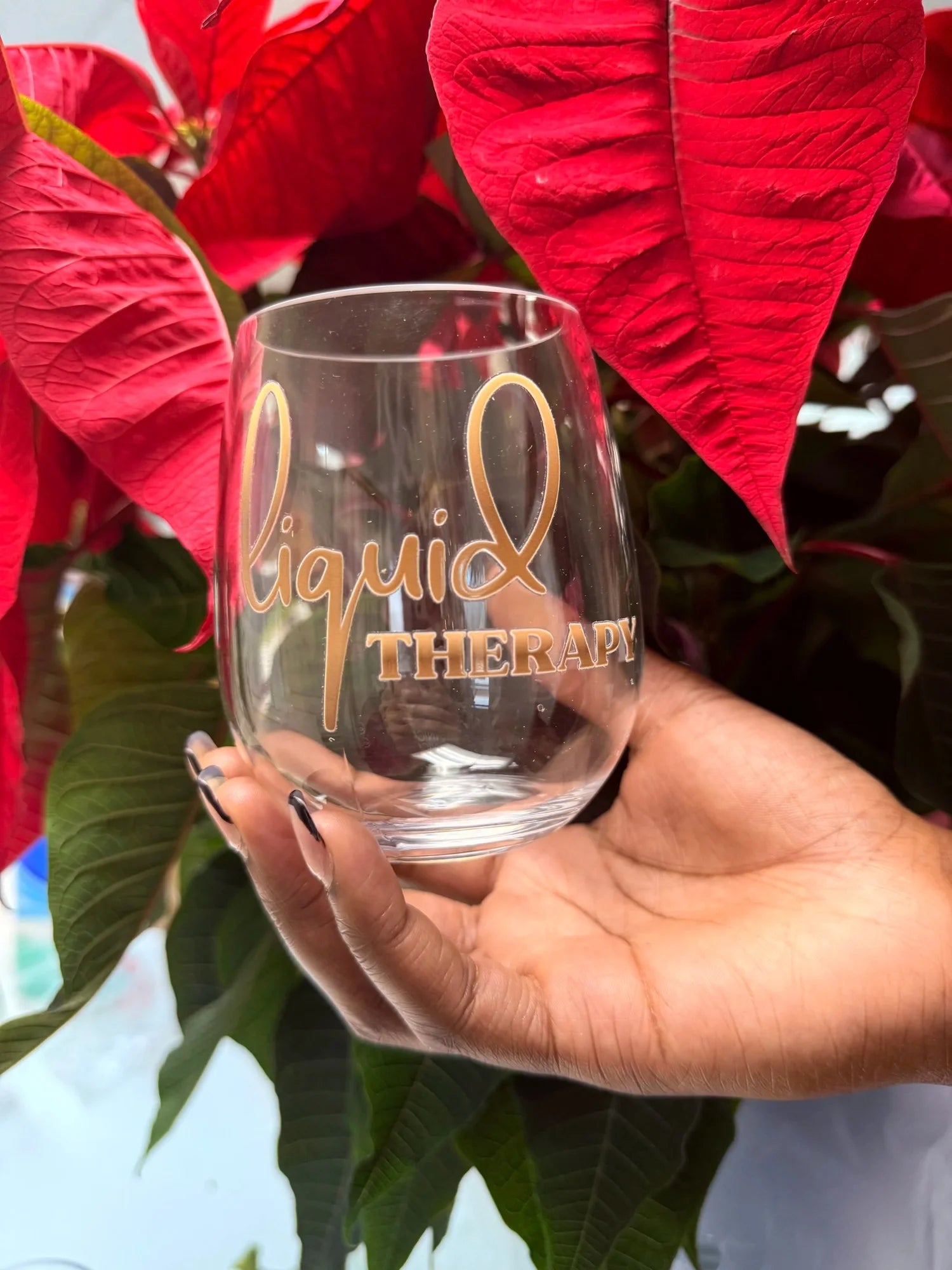 A clear stemless wine glass with the words 'liquid therapy' printed on it in colorful gradient lettering, set against a neutral beige and white background.

