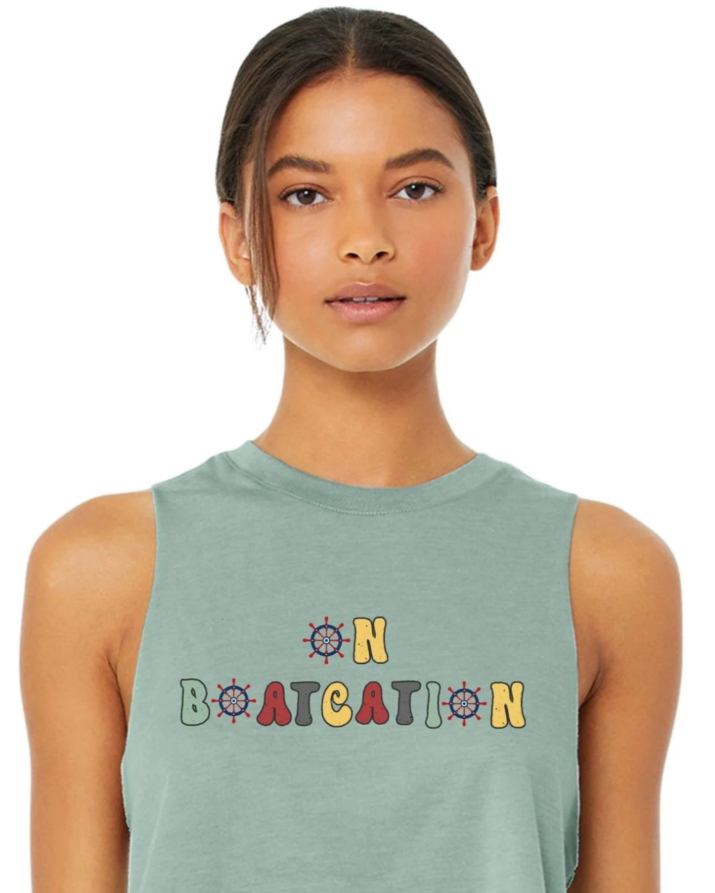A woman wearing a sage green sleeveless muscle tank top with a colorful retro-style graphic that reads 'ON BOATCATION' on the chest, set against a plain white background.