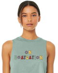 A woman wearing a sage green sleeveless muscle tank top with a colorful retro-style graphic that reads 'ON BOATCATION' on the chest, set against a plain white background.