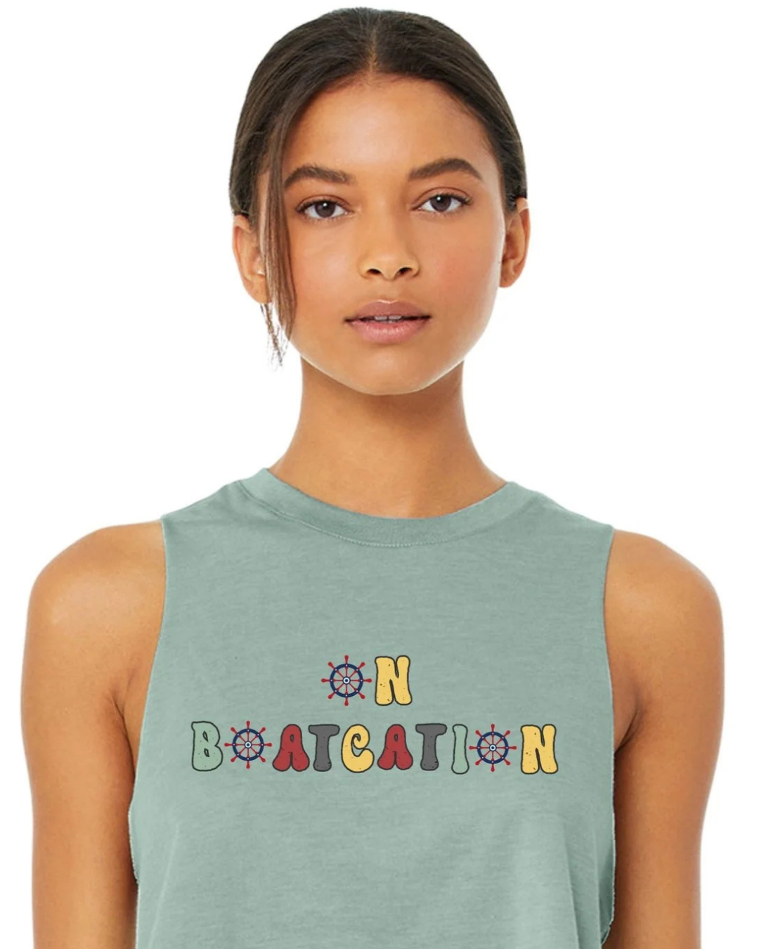 A woman wearing a sage green sleeveless muscle tank top with a colorful retro-style graphic that reads 'ON BOATCATION' on the chest, set against a plain white background.