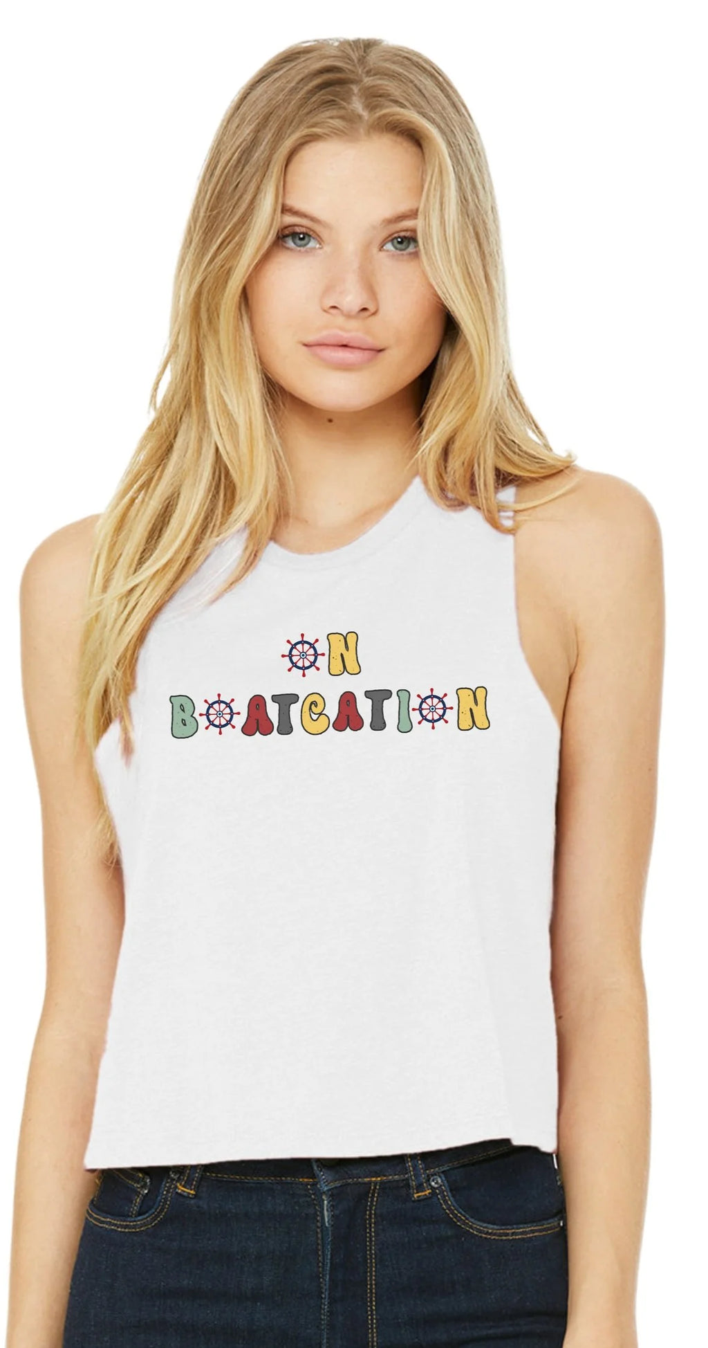 A blonde woman wearing a white sleeveless crop top with a colorful retro-style graphic that reads 'ON BOATCATION' and dark blue jeans, photographed against a plain white background.