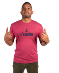A man wearing a heathered pink t-shirt with a navy blue graphic that reads 'el capitán' with an anchor icon, posing with his hands raised against a plain white background.