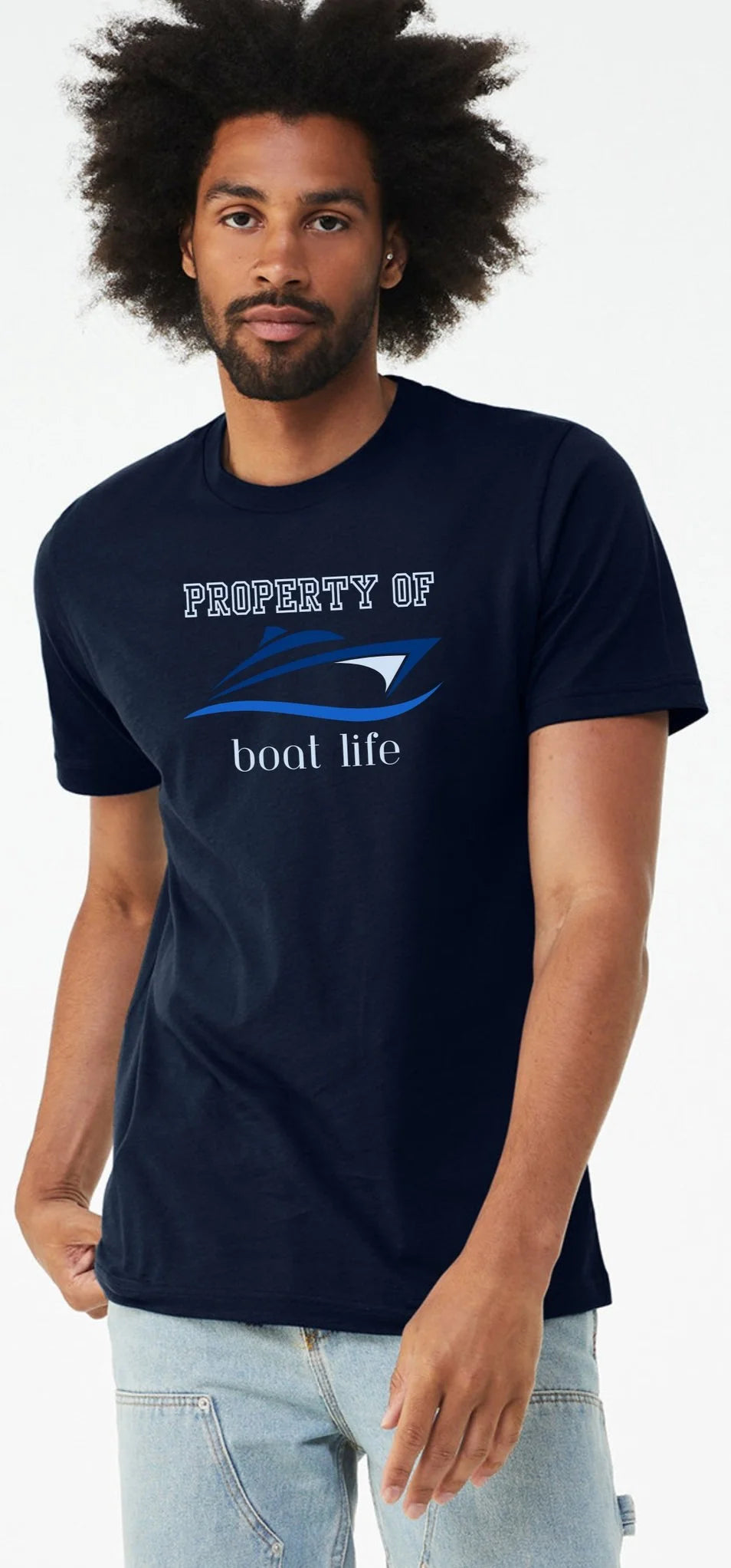 A man wearing a navy blue crewneck t-shirt with a boat graphic that reads 'PROPERTY OF boat life' and a blue wave design, paired with light wash jeans, against a plain white background.