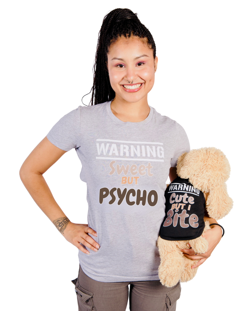 A smiling woman holding a plush dog toy wearing a matching black shirt with the text 'WARNING Cute But I Bite'. The woman wears a light gray t-shirt that reads 'WARNING Sweet BUT Psycho'.
