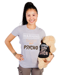 A smiling woman holding a plush dog toy wearing a matching black shirt with the text 'WARNING Cute But I Bite'. The woman wears a light gray t-shirt that reads 'WARNING Sweet BUT Psycho'.