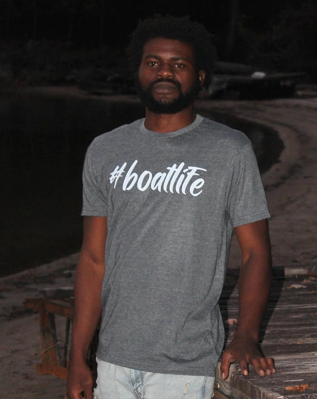 A man wearing a heather gray t-shirt with the white text '#boatlite' printed across the chest, standing outdoors on a wooden dock at night.